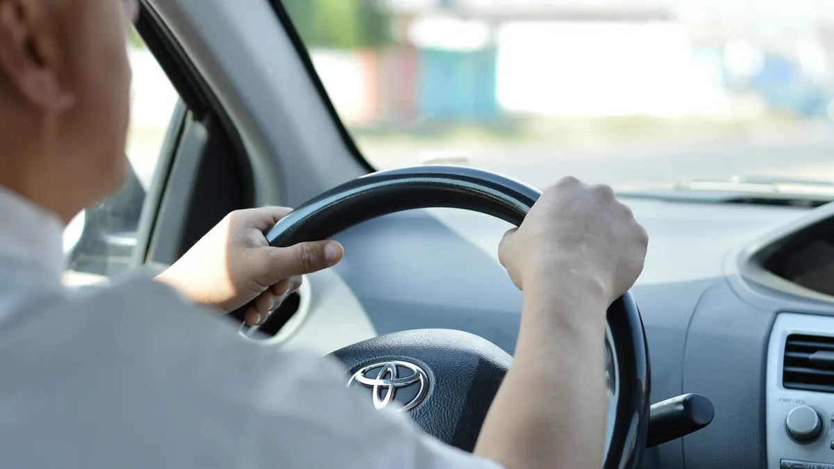 Close-up of a driver's hands on a car steering wheel during a daytime drive