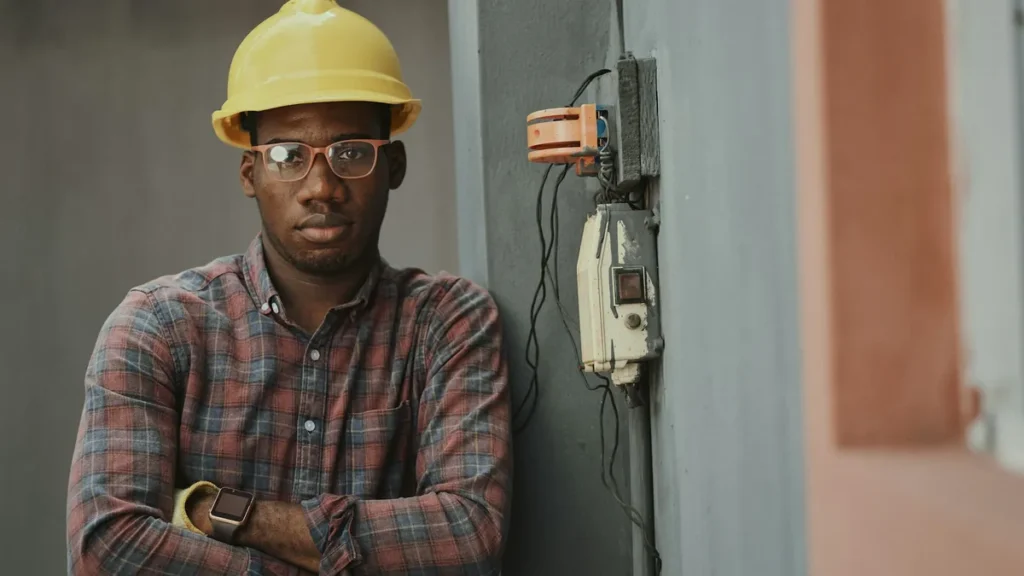 Worker in a yellow hard hat standing by an electrical panel on a work site