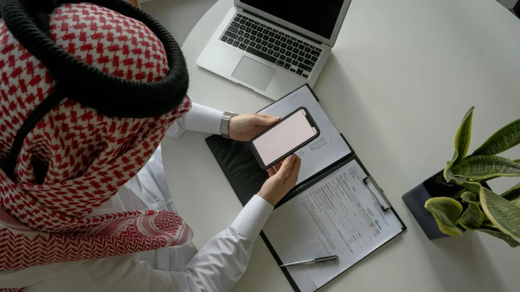 رجل سعودي يراجع عقد العمل على ملف أوراق وهاتفه قبل توثيقه في منصة قوى