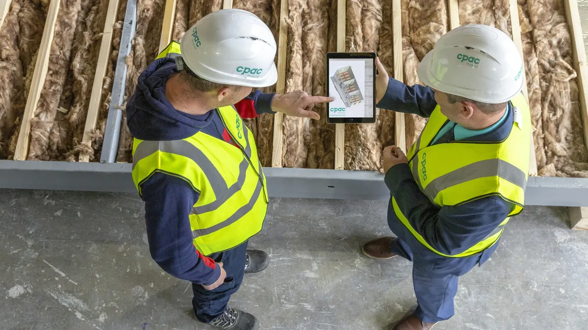 Two site engineers in hard hats reviewing plans on a tablet